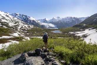 Hiker enjoys views from Portage Pass of Divide Lake, snowy mountain peaks and glaciers Portage