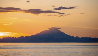 View of Cook Inlet on white mountain peaks of Mount Redoubt at sunset, picturesque golden light of