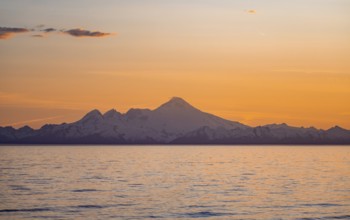 View of Cook Inlet on white mountain peaks of Mount Iliamna at sunset, picturesque golden light of