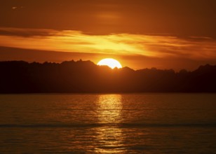 Sun sets behind mountain peaks, view of Cook Inlet at sunset, picturesque golden light of the