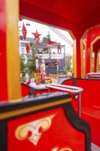 Red train at a Christmas market with festive decorations and fir trees in the background,