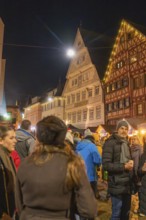 People enjoy a Christmas market evening surrounded by half-timbered houses and atmospheric lights,