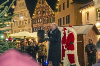A man gives a speech next to Santa Claus on a market square with half-timbered houses, Christmas