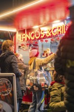 People stand at a red-lit food stand at a Christmas market, Christmas market 2025, Nagold, Black