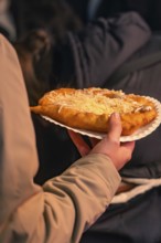 Hand holding a plate of warm pastries sprinkled with cheese at a party, Christmas market 2025,