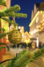 Golden Christmas ball on a pine branch surrounded by blurred lights, Christmas market 2025, Nagold,