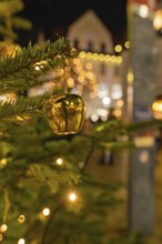Close-up of a golden Christmas ornament on a pine branch with lights in the background, Christmas