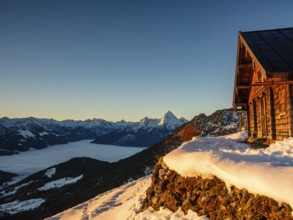 Alpine hut in winter at morning light, behind the Watzmann, fog in the valley, Berchtesgaden Alps,