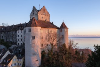 The historic Meersburg Castle, illuminated by the setting sun, right behind it Lake Constance with
