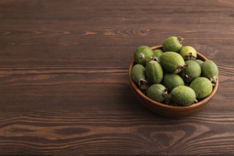 Ripe Feijoa in wooden bowl on brown wooden background, side view, copy space, minimalism