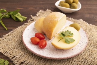 Smoked Mozzarella cheese, with tomatoes and olives on brown wooden background and linen textile,