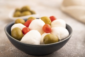 White Mozzarella cheese, with tomatoes and olives in blue bowl on brown concrete background and