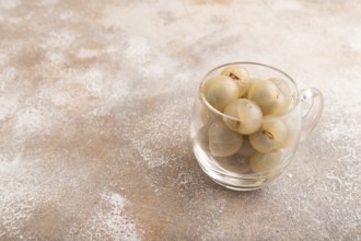 Ripe peeled Longan in glass on brown concrete background, side view, copy space, minimalism