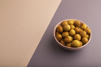 Ripe Longan in ceramic bowl on brown and gray pastel paper background, side view, copy space,