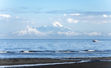 View over Cook Inlet to white mountain peaks of Mount Iliamna, motor boat rides on the ocean,