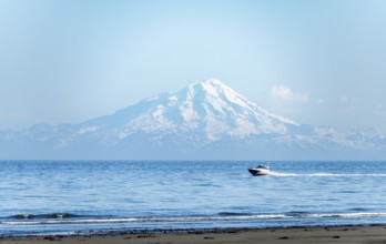 View over Cook Inlet to white mountain peaks of Mount Redoubt, motor boat rides on the ocean,