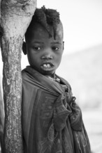 Black and white, Himba girl leaning at a traditional clay hut, in the morning, traditional Himba