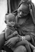 Black and white baby in the arms of a Himba woman, traditional Himba village, Kaokoveld, Kunene,