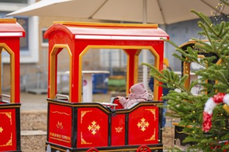 A child sits on a red miniature train next to a Christmas tree at a market, Sindelfingen, Böblingen