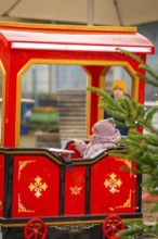 Little girl sitting on a red toy train at a Christmas market, Sindelfingen, Böblingen district,