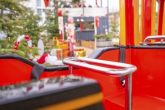 Close-up of a Christmas carousel ride with red and yellow seats in front of a decorated tree,