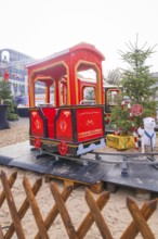 Colourful children's train on rails next to Christmas tree and fences on market, Sindelfingen,