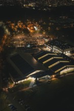 Aerial view of an illuminated building structure at night with surrounding parking spaces,