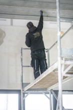 A worker stands on scaffolding and works on the ceiling in a renovated room, electrician, new