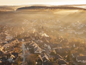 Fog-covered village with church tower in morning light with surrounding hills and mountains,
