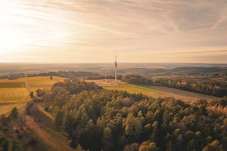 Radio tower in the middle of a vast landscape surrounded by forests in soft evening light,