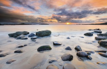 Orange cloudy sky at sunset on a sandy beach with round stones near Achiltibuie on the west coast