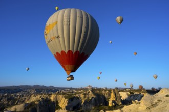 Large hot air balloon soars over a vast, rocky landscape under clear skies, Göreme National Park,