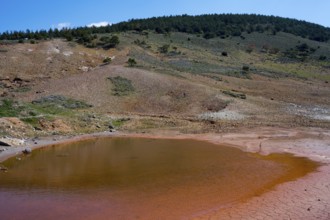 Small red lake in a geological mountain landscape under blue sky, geothermal area, rainbow rocks