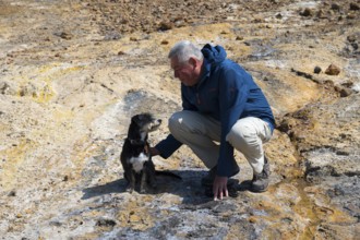Man playing with dog in a rocky, natural environment, dressed in outdoor clothing, dog and man