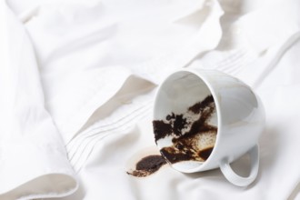 A white cup with the remains of coffee, spilled, lies on a white shirt, there are no people, a soft