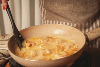 In a cozy kitchen, a person is stirring shrimp in a creamy sauce on the stove. The scene captures