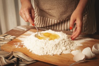 In a warm kitchen, hands mix fresh eggs into a mound of flour on a wooden surface. The process is