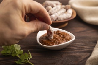 Small smoked Chicken sausages in wooden bowl with hand on brown wooden background and linen textile