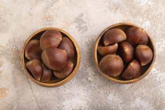 Wooden bowl with raw edible Ð¡hestnuts on brown concrete background, top view, flat lay, close up,