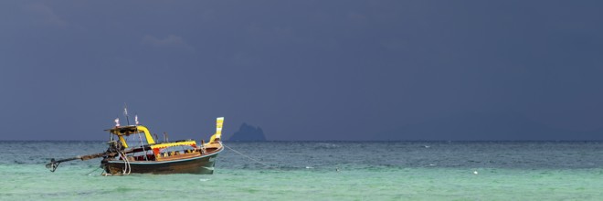 Longtail boat (Thai: Ruea Hang Yao) on the beach, behind it an approaching thunderstorm, Koh Ngai