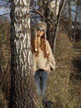 Slender pretty woman with fur hat and sweater, red hair and warm winter colors between birch forest