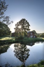 Manor with historic stable and pond, from 1923, in backlight with sun star, Gut Othenstorf,