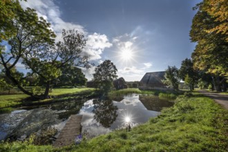 Manor with historic stables and pond, from 1923, in backlight with sun star, Gut Othenstorf,