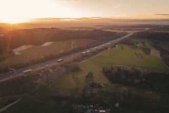 Highway in a vast landscape at sunrise, fields and forests in soft morning light, A8 motorway,