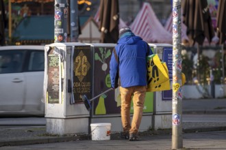 Man sticks posters to electrical boxes near Alexanderplatz, Berlin, Germany