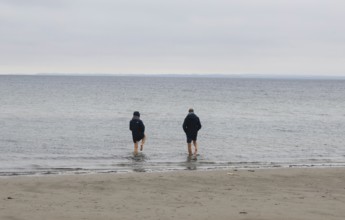 A couple standing barefoot in the cold seawater of the Baltic Sea, Scharbeutz, 28.11.2025,