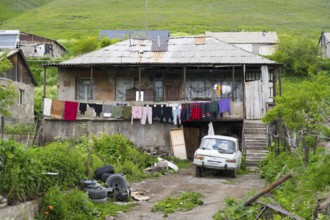 Rural house with clothesline and old car nestled in green landscape with hills, poor house in