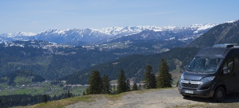 A van parks with a view of a snowy mountain landscape and green forests, camper, view from Goderdzi