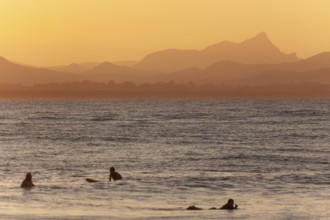 Red sunset on Wategos Beach with surfers in the ocean. Mt. Warning, Wollumbin in the background of
