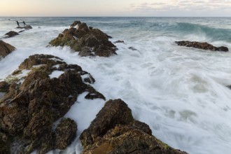 The Cape Byron Lookout at high tide: rocks and anglers in golden light. Byron Bay, New South Wales,